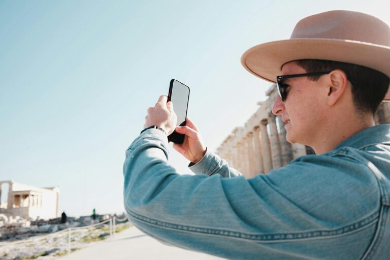 Young man takes a smartphone photo of the Parthenon, showcasing modern tourism at historic site.